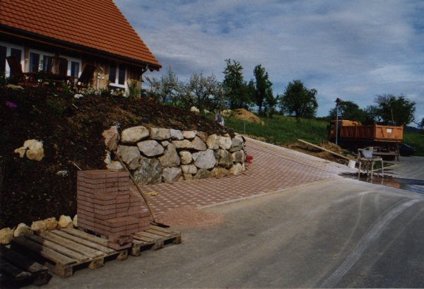 Fertig verlegte Verbundsteine mit Natursteinmauer zur Hangsicherung
